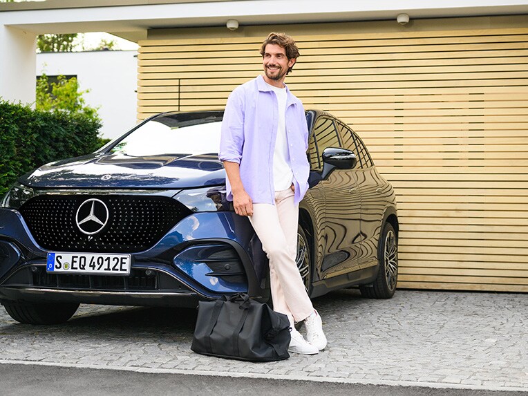 A person leaning against a Mercedes-Benz vehicle looking at the sky.