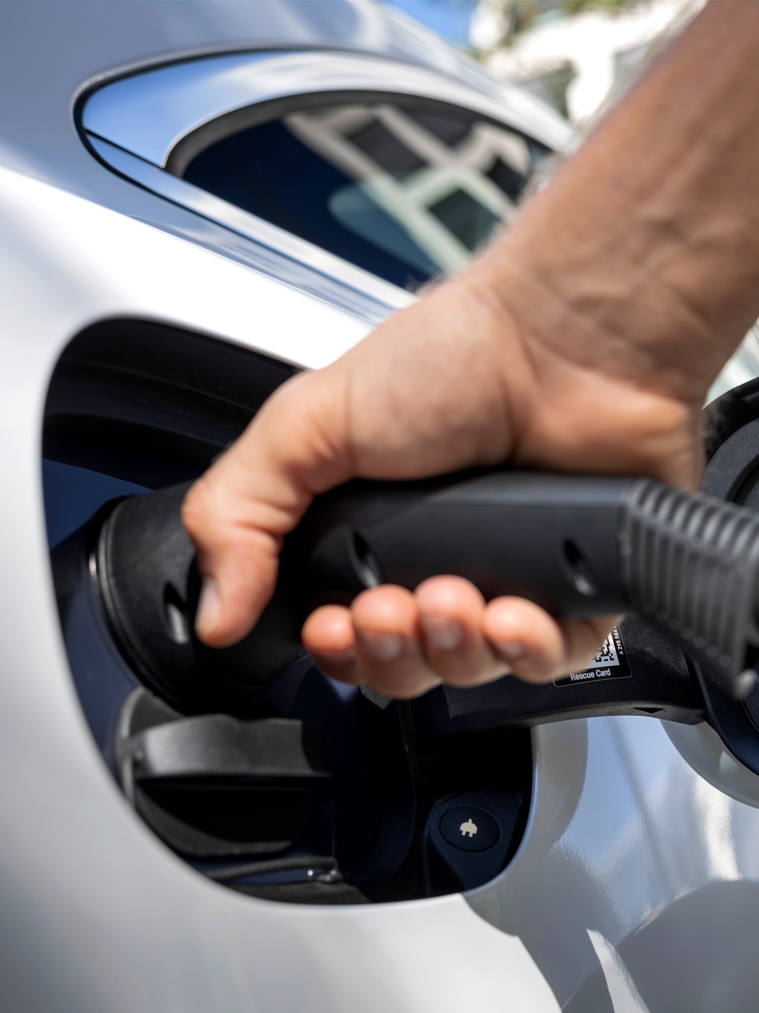 A hand holding a type 2 connector that is connected to an electric car